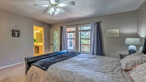 A bedroom with a large bed, a ceiling fan, a window with curtains, and a bathroom visible through an open door.