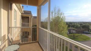 Un balcon avec une table et des chaises, une vue sur un parking et un bâtiment en arrière-plan.