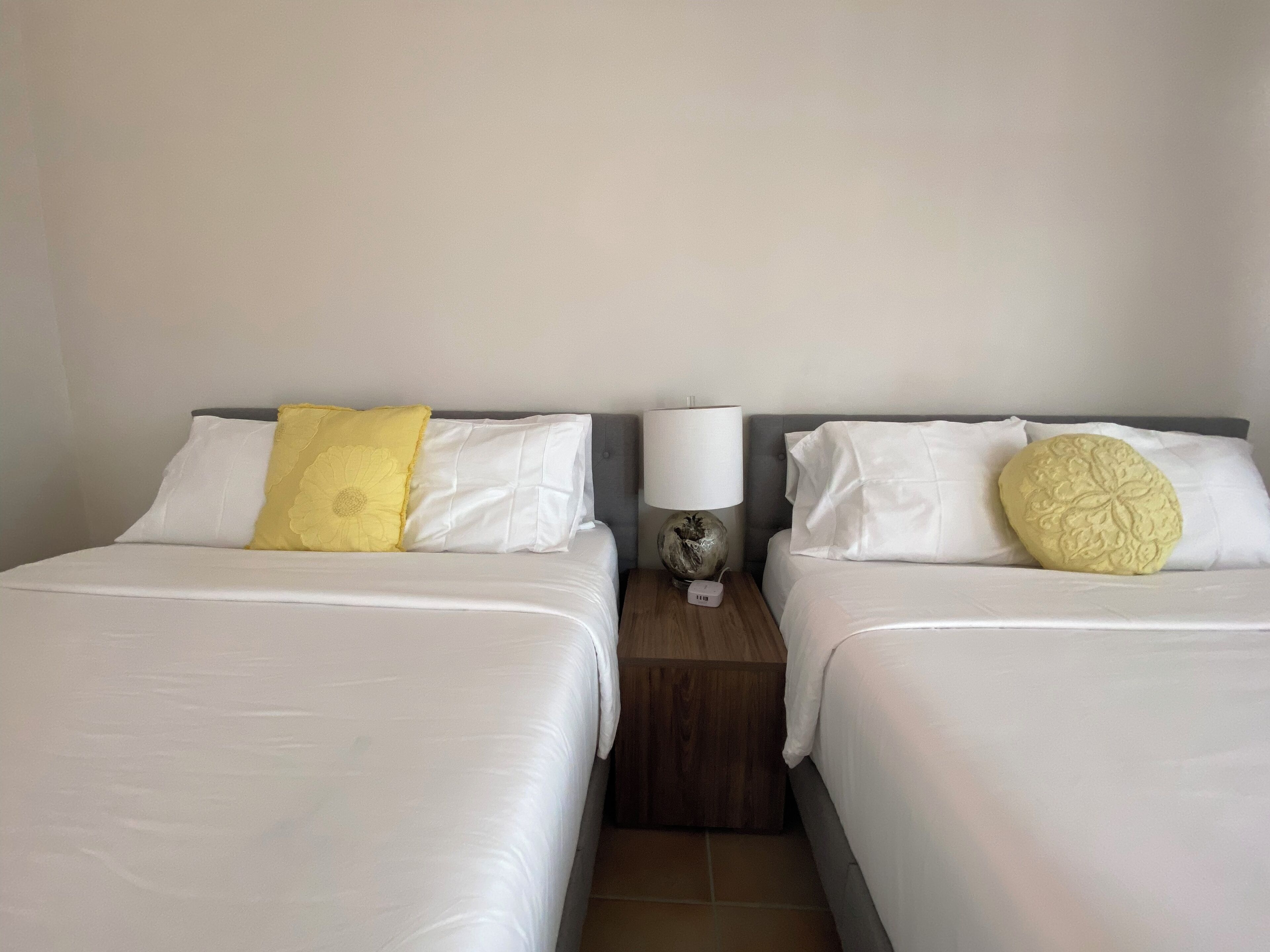 Zwei Betten mit weißen Laken, ein Nachttisch mit einer Lampe und auf jedem Bett ein Zierkissen.
