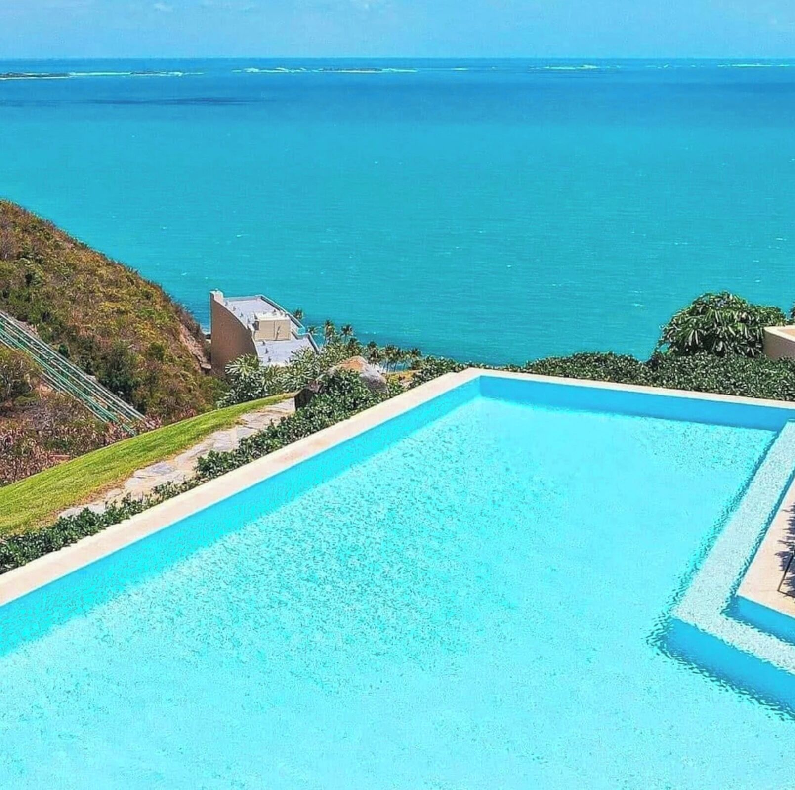Une piscine rectangulaire à l’eau d’un bleu cristallin, entourée d’un espace paysager offrant une vue sur l’océan.