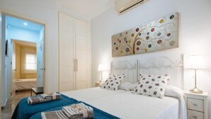 A hotel room with a large bed, two bedside tables, a wall-mounted air conditioner, and a decorative painting. - Duplex Sweet Home by SevillaLuxurySuites (Sevilla)