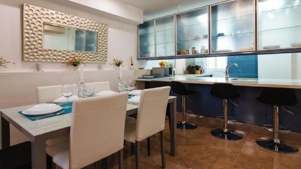 A modern dining area with a white table set for four, a large mirror with a decorative frame, and a blue-tiled backsplash. - Duplex Sweet Home by SevillaLuxurySuites (Sevilla)
