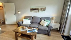 Ein Wohnzimmer mit grauem Sofa, einem Couchtisch mit Zeitschriften, einer Lampe und einem Bild an der Wand.