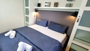 Ein ordentlich gemachtes Bett mit gestreifter Bettwäsche und zwei Kissen, ein Nachttisch mit Lampe sowie ein Regal mit Dekoration.