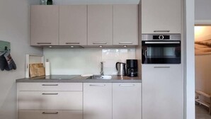 Eine kleine Küche mit hellen Schränken, einer Edelstahl-Spüle, einer Kaffeemaschine und einem Backofen.