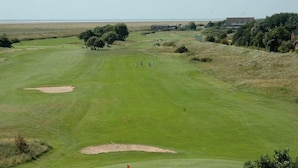 Un campo da golf con bunker, alberi e un edificio in lontananza.