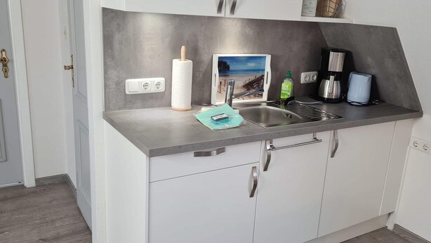 A modern kitchen with a built-in sink, a coffee maker, and a picture frame on the countertop. - App. Liebrecht OG Links (St. Peter-Ording)