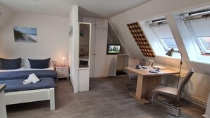 A bedroom with a bed, bedside tables, a desk, and a chair. There is a window with curtains and a skylight. - App. Liebrecht OG Links (St. Peter-Ording)