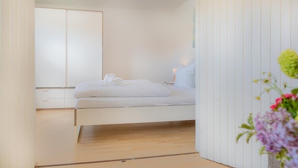 A minimalist bedroom with a bed, a nightstand, and a mirror. - Wohnung A (St. Peter-Ording)