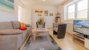A modern living room with a sofa, a coffee table, a TV, and a bookshelf. - Wohnung A (St. Peter-Ording)