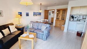 A living room with a black sofa, a striped sofa, a coffee table, and a dining area with chairs and a table. - Haus Quisisana Fewo Nr.22 (St. Peter-Ording)