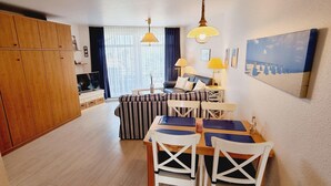 A compact living space with a dining area, a sofa, a TV, and a wooden wardrobe. - Haus Quisisana Fewo Nr.22 (St. Peter-Ording)