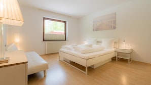 Ein modernes Schlafzimmer mit Bett, Nachttischen, einer Bank, einem Fenster und einer Heizung.