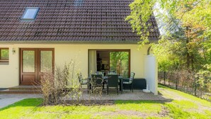 Ein Haus mit Ziegeldach, einer Haustür und einer Terrasse mit Gartenmöbeln.