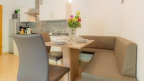 Ein stilvoller Essbereich mit einem Holztisch, zwei grauen Stühlen und einem beigen Sofa. Auf dem Tisch steht eine Vase mit Blumen, und im Hintergrund ist eine Küche erkennbar.