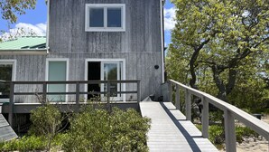 Un edificio su due piani con facciata in legno, una zona esterna coperta e una scala in legno che conduce all'ingresso.