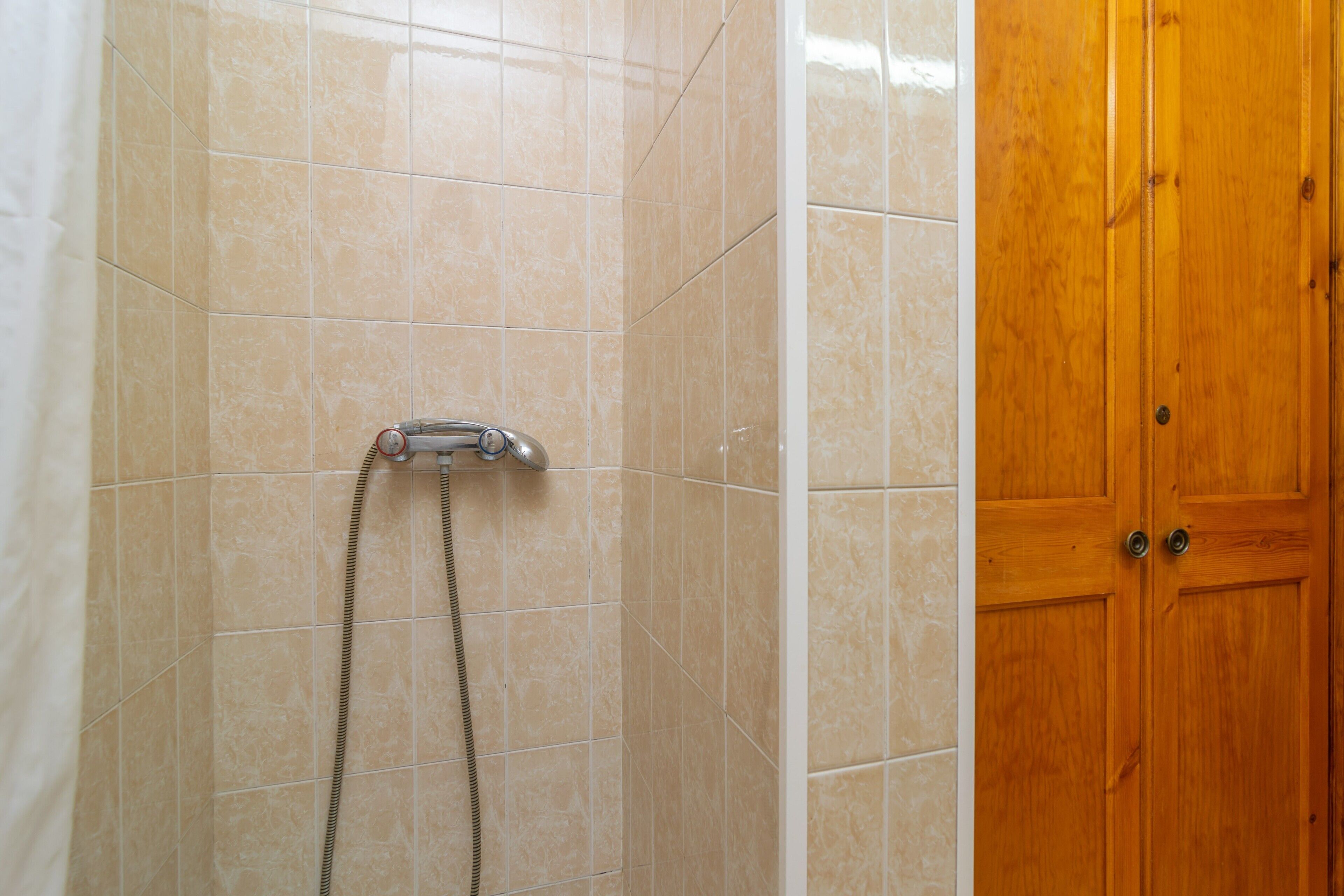 Un baño con azulejos color beige, un cabezal de ducha y una puerta de madera.