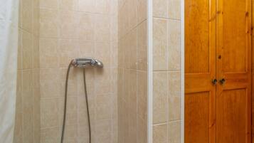 Un baño con azulejos color beige, un cabezal de ducha y una puerta de madera.