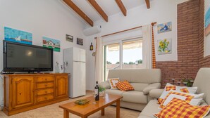 A living room with a television, wooden cabinet, sofa, and a window with curtains.