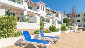 A resort with white buildings, balconies, and blue lounge chairs.