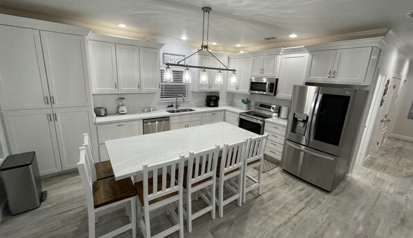 Una cocina moderna con armarios blancos, electrodomésticos de acero inoxidable y una isla central con taburetes de bar.