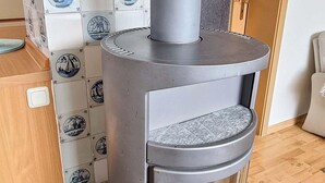A modern wood-burning stove with a glass door, a firebox, and a chimney. - Ferienhaus "deister" (St. Peter-Ording)