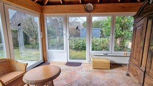 A sunroom with large windows, wicker furniture, and a wooden cabinet. - Ferienhaus "deister" (St. Peter-Ording)
