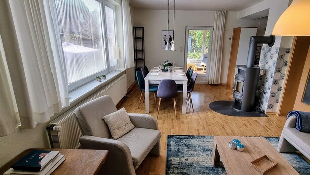 A cozy living room with a sofa, a dining table, and a fireplace. - Ferienhaus "deister" (St. Peter-Ording)