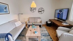 A modern living room with a sofa, armchairs, a coffee table, a TV, and decorative wall art. - Ferienhaus "deister" (St. Peter-Ording)