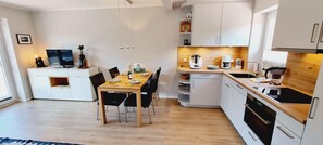 Moderni keittiö, jossa on valkoiset kaapit, puinen ruokapöytä ja televisio nurkassa.