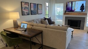 A living room with a sofa, a coffee table with a laptop, a TV, and a fireplace. - Boutique Condo in North Scottsdale (Scottsdale)