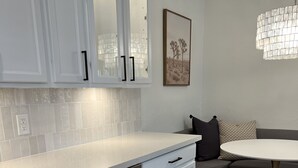 A modern kitchen with white cabinetry, a built-in dishwasher, and a round dining table with a gold base. - Boutique Condo in North Scottsdale (Scottsdale)