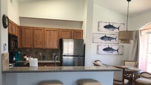 A kitchen with wooden cabinets, a stainless steel refrigerator, a coffee maker, and a dining area with wicker chairs and a small table.