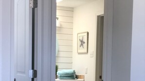 A narrow hallway leading to a bathroom with wooden cabinets and a towel rack.