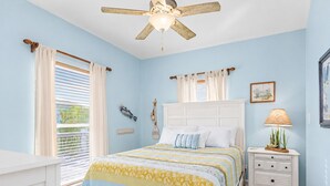 A bedroom with a bed, a nightstand, a ceiling fan, and a window with curtains.