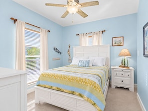 A bedroom with a bed, a nightstand, a ceiling fan, and a window with curtains.
