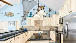 A spacious kitchen with white cabinets, a stainless steel refrigerator, and a large island.