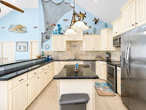 A spacious kitchen with white cabinets, a stainless steel refrigerator, and a large island.