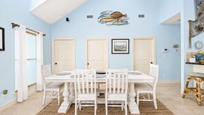 A dining room with a white table and chairs, light blue walls, and a ceiling with a skylight.