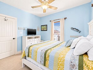 A bedroom with a bed, a television on a dresser, a ceiling fan, and a window with curtains.