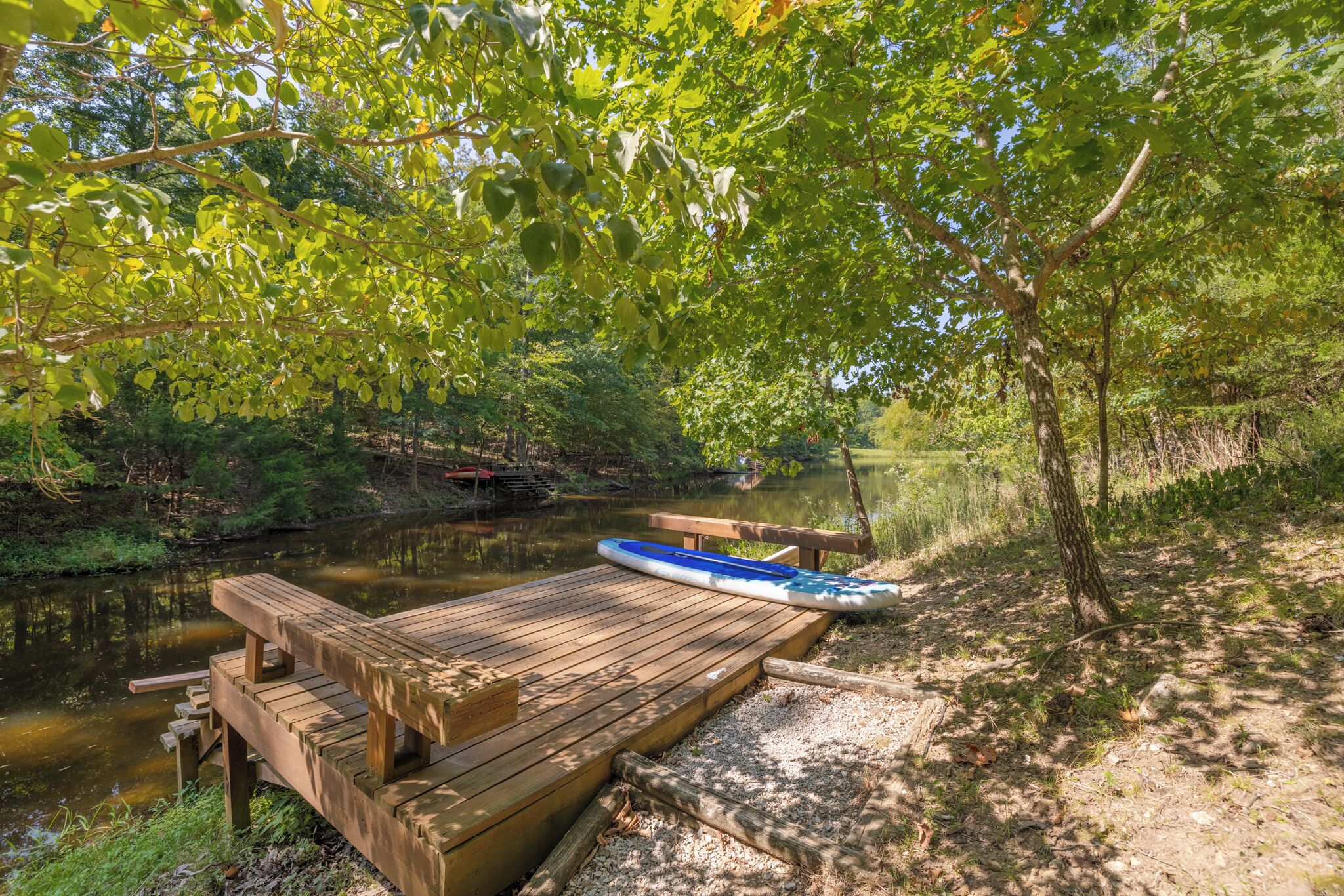 Un muelle de madera se extiende sobre un río tranquilo, rodeado de exuberante vegetación y árboles.