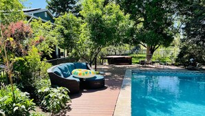 Una piscina con plataforma de madera, rodeada de vegetación exuberante y árboles.
