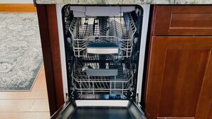 Un lavavajillas Bosch abierto en una cocina con encimera de granito, armarios de madera y un salpicadero con diseño.