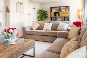 A living room with a beige sectional sofa, a wooden coffee table, a bookshelf, and a potted plant. - Homestead, Southrepps, Norfolk (Southrepps)