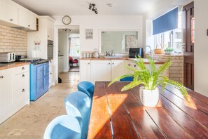 A compact kitchen with a dining area, a clock, and a potted plant.