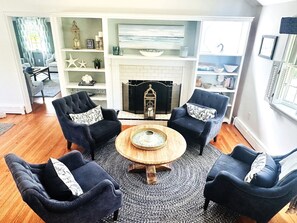 Un salon avec une cheminée, deux fauteuils, une table basse et une bibliothèque.