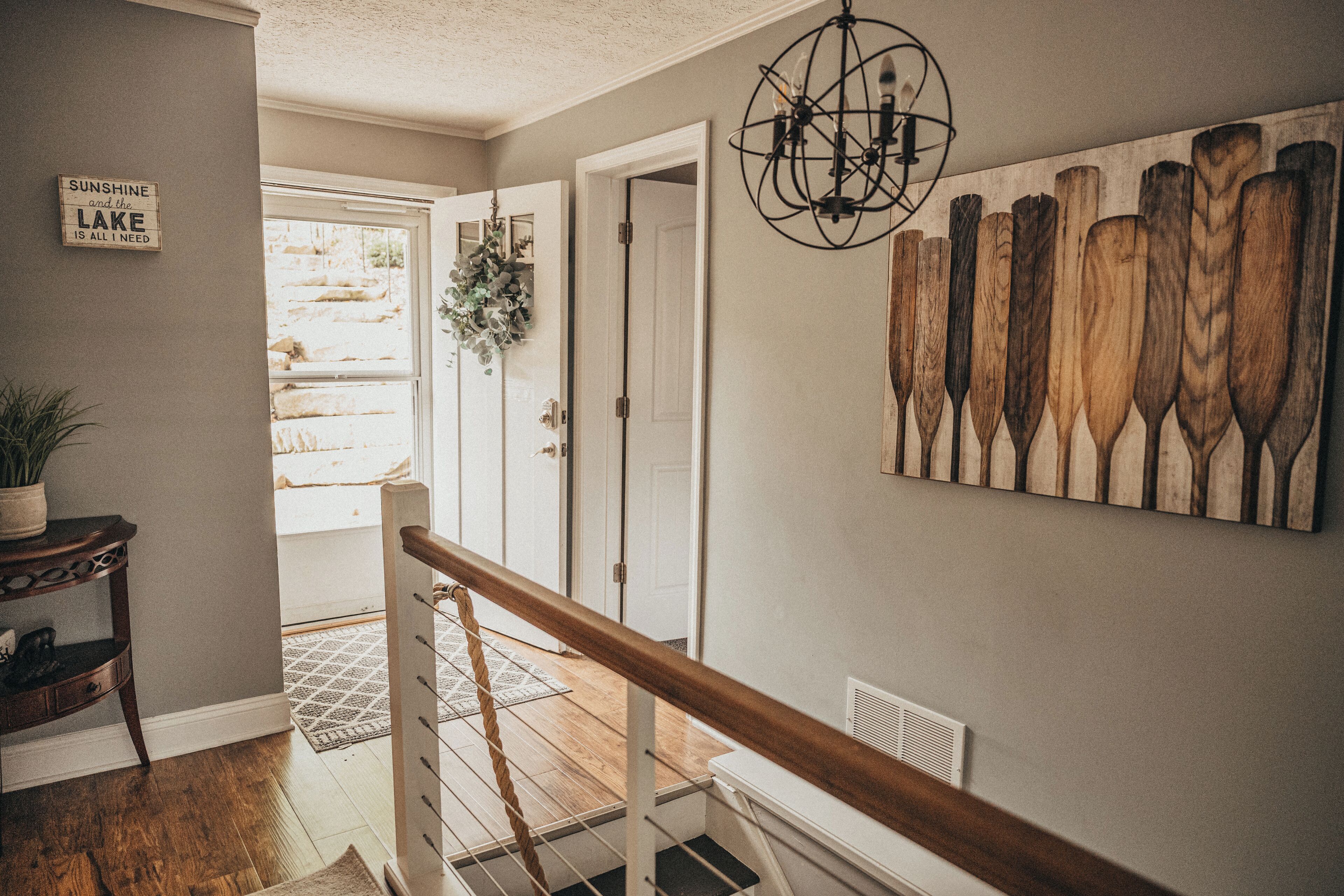 Un escalier avec une rampe en bois menant à une pièce dotée d’une porte, d’un luminaire fixé au mur et d’une enseigne avec du texte.