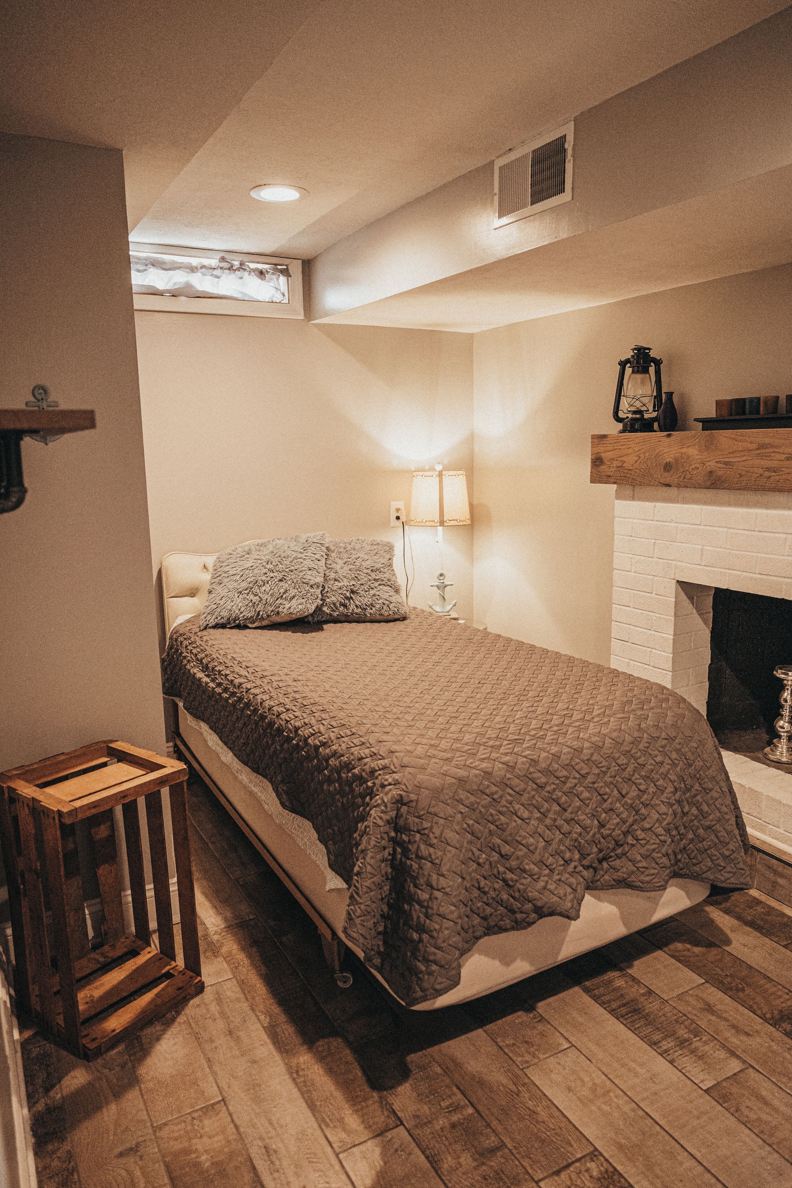 Ein Schlafzimmer mit einem Bett, einem Nachttisch aus Holz, einer Lampe, einem Kamin und einem Fenster.