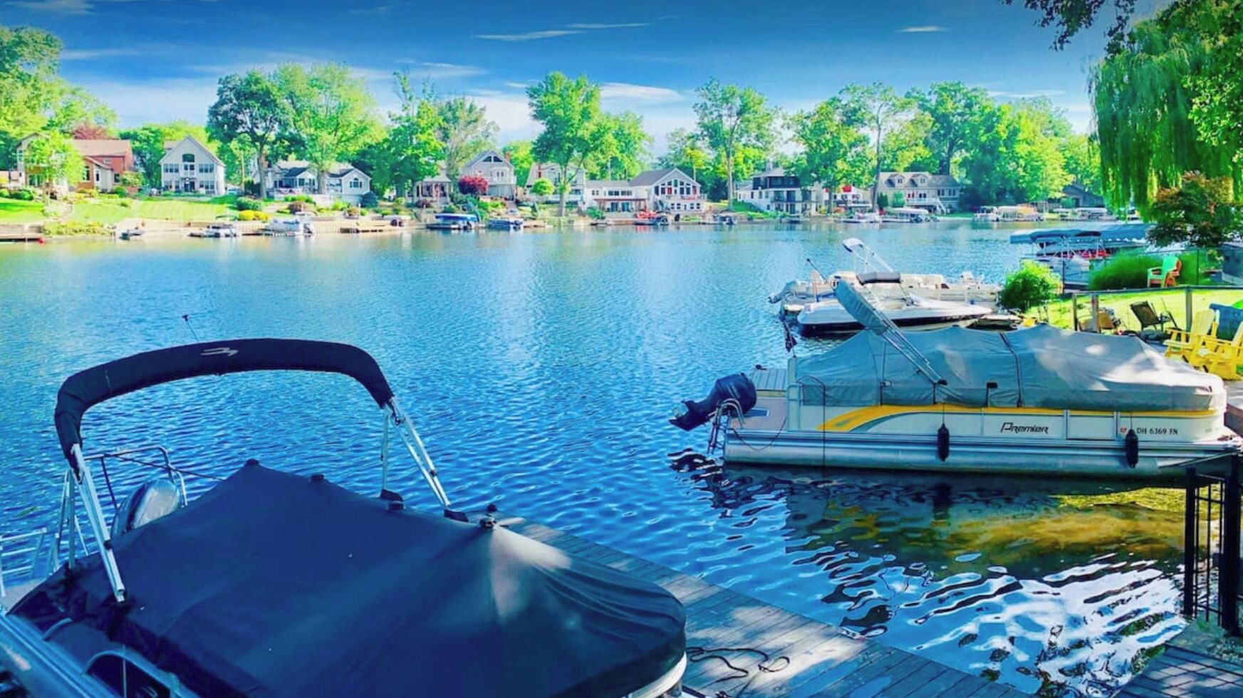 Un barco amarrado con una zona de estar cubierta, un muelle flotante y vistas a una zona residencial con casas y árboles al otro lado del agua.