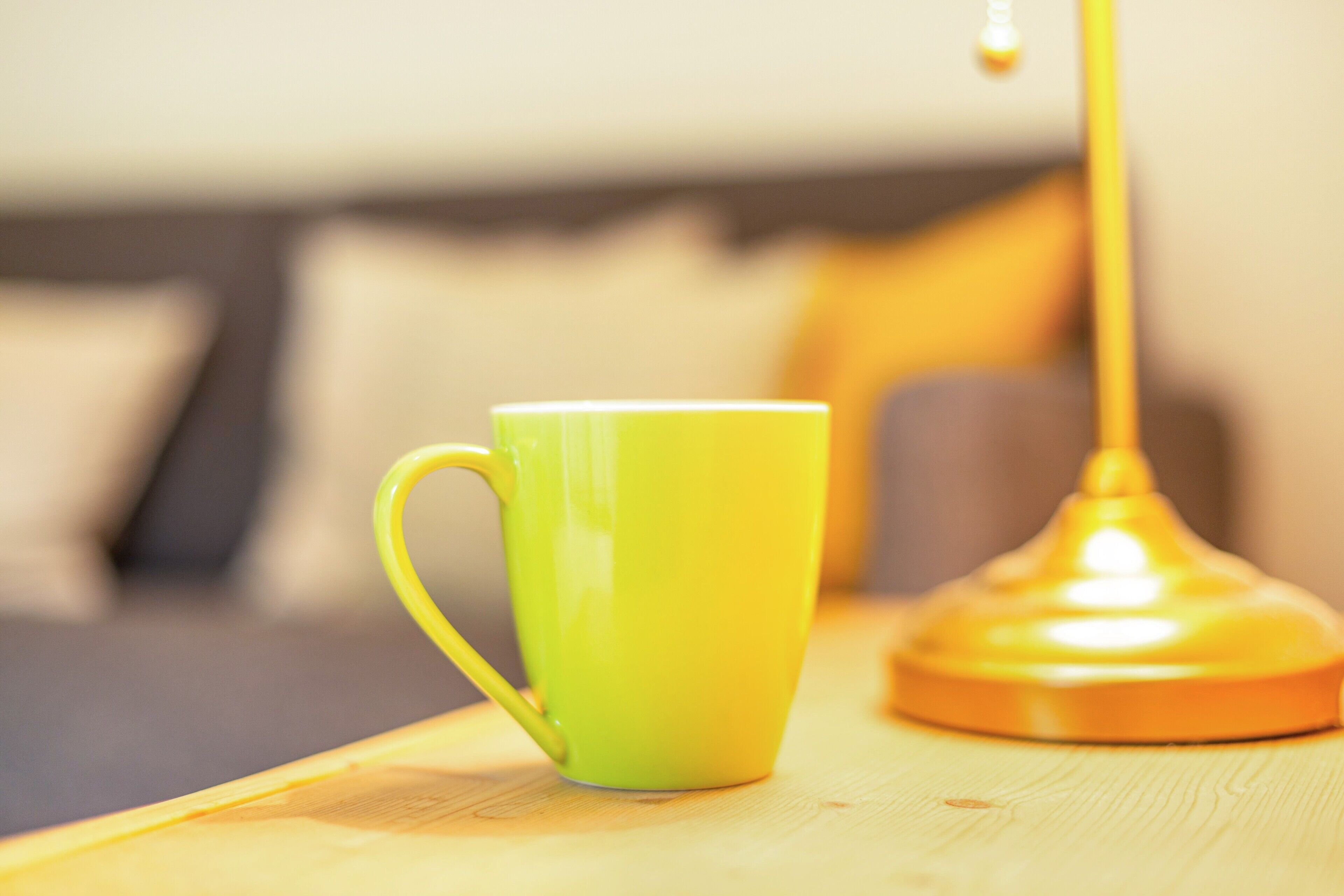 Una taza verde sobre una superficie de madera, con una lámpara al fondo.